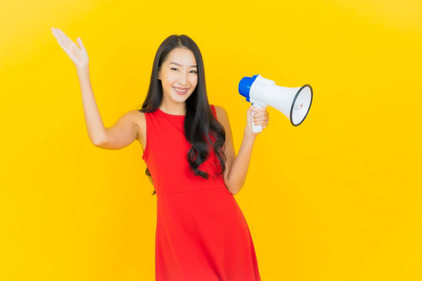 Retrato hermosa joven mujer asiática sonrisa con megáfono sobre fondo de color amarillo - Foto, imagen