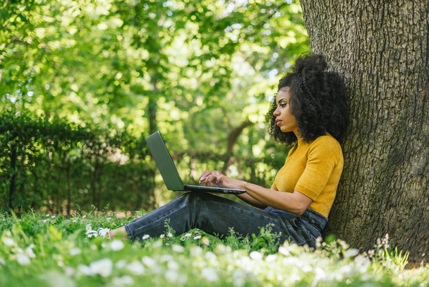 庭のノートパソコンに入力する美しいアフロ女性. - 写真・画像