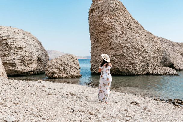 Woman in elegant long white summer dress standing on beautiful Beritnica beach with large rock formations on Pag island in Croatia. - Foto, Bild