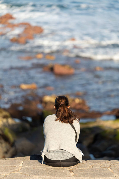 A rear view of a lonely woman sitting on a rocky surface - Zdjęcie, obraz