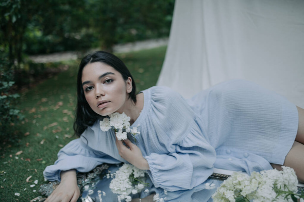 ritratto di una bella giovane donna in posa davanti alla macchina fotografica con dei fiori in un parco - Foto, immagini