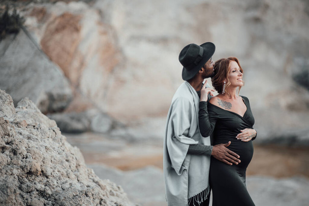 afro-amerikai férfi ölelés terhes nő fekete ruhában, pár pózol gránit kanyon - Fotó, kép