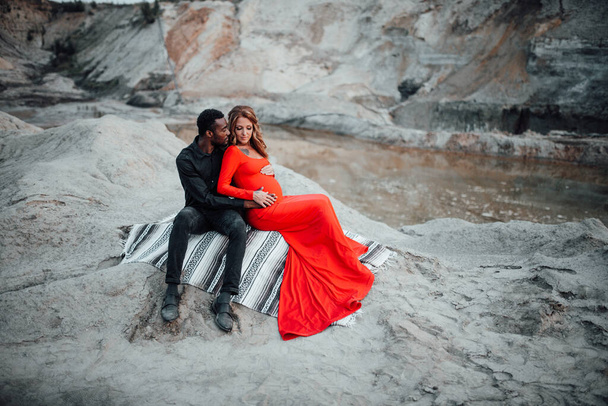  multi casal étnico posando contra o cânion de granito. Mulher grávida vestindo elegante vestido vermelho  - Foto, Imagem