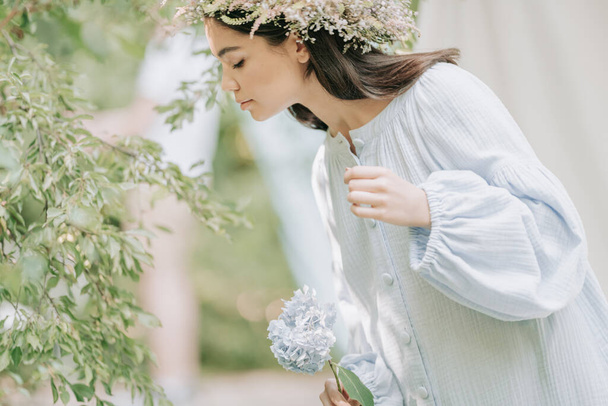 jeune femme en couronne de fleurs posant à la caméra avec des fleurs d'hortensia à la main  - Photo, image