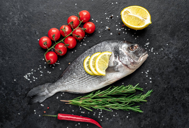 raw fish with lemon and rosemary on black stone background. top view. - Photo, Image