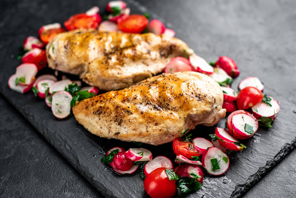 grilled chicken breasts with vegetables and spices on a black background. - Photo, Image