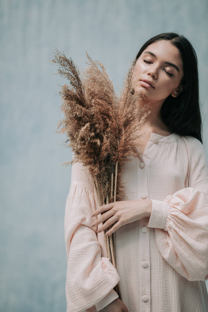 brunette woman posing with dried flowers in pink dress against cloth background  - Fotoğraf, Görsel