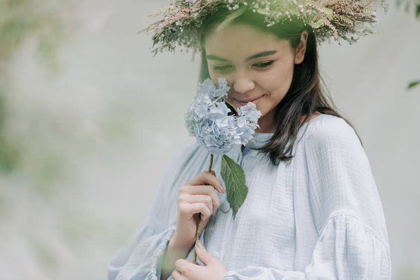 aantrekkelijke vrouw in bloem krans poseren op camera met hortensia bloemen  - Foto, afbeelding