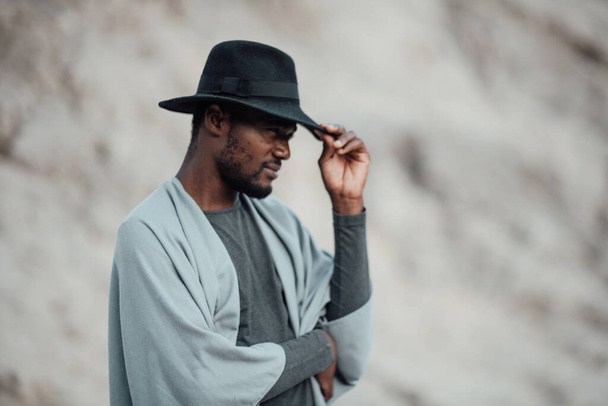 Porträt eines afrikanisch-amerikanischen Mannes mit Fedora-Hut, der vor einer Granitschlucht posiert  - Foto, Bild