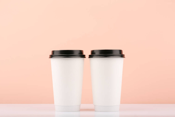 コピースペース付きベージュの背景を持つ2つの白い使い捨てコーヒーまたはティーカップ - 写真・画像