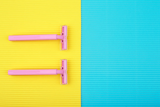 Top view of pink razors against yellow and blue background with space for text - Фото, изображение