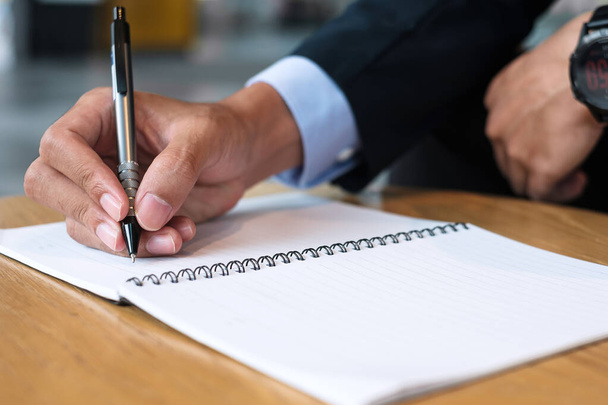 Επιχειρηματίας με κοστούμι γράφει κάτι στο σημειωματάριο στο γραφείο ή καφέ, χέρι του ανθρώπου κρατώντας στυλό με υπογραφή σε χαρτί έκθεση. επιχειρηματικές έννοιες - Φωτογραφία, εικόνα