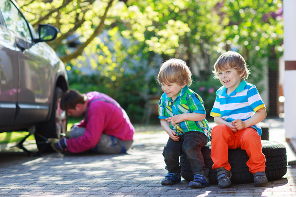 Отец и двое маленьких мальчиков ремонтируют машину и меняют колесо.
 - Фото, изображение
