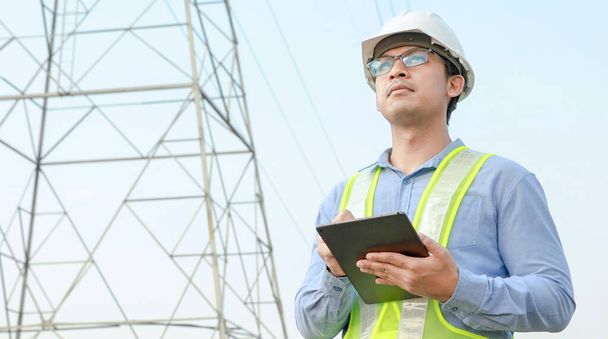 electrical engineer working on digital tablet with electric power pole background - Photo, Image
