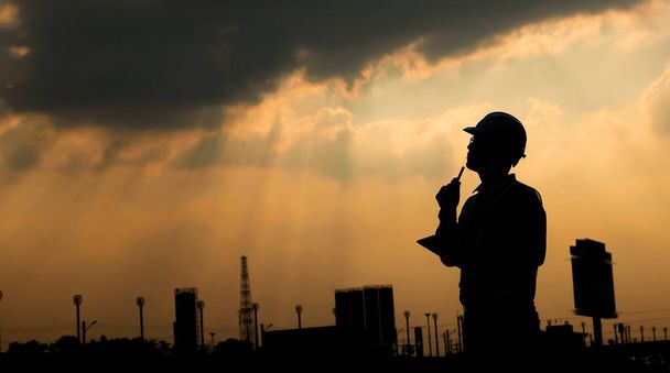 Engineer talk on mobile phone at construction site at sunset silhouette - Photo, Image