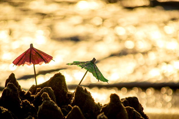 Két kis tengerparti esernyő, koktélpapírból, homokban, homokban, homokban. - Fotó, kép