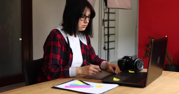 Creatieve vrouwelijke fotograaf, gebruikmakend van grafische tekentablet en stylus pen, werkend aan bureau en retoucheren foto op laptop, Retoucheerplek in fotostudio - Video
