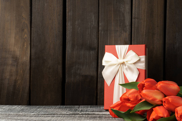 boeket tulpen op een donkere houten achtergrond met een geschenkdoos en kopieerruimte. Briefkaart voor de feestdagen. Feestelijke template. - Foto, afbeelding
