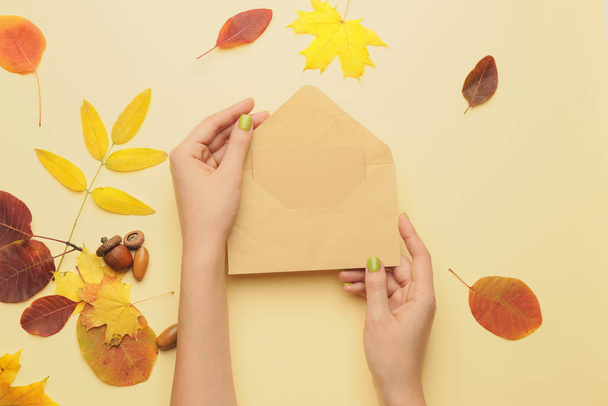 Female hands with envelope, blank card and autumn leaves on color background - 写真・画像