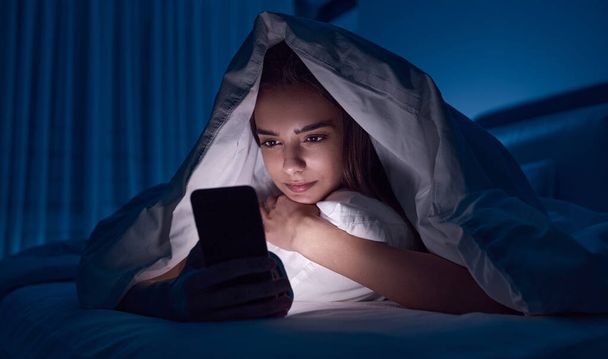 Young woman using smartphone in bed - Foto, Bild