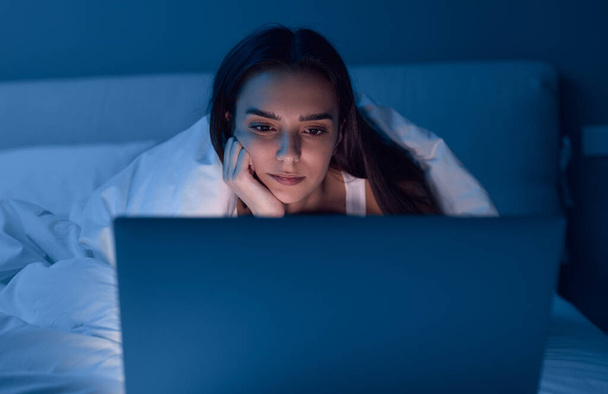 Bored woman watching movie on bed at night - Valokuva, kuva