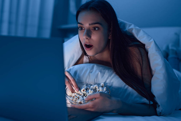 Astonished woman with popcorn watching movie on bed - Foto, Bild