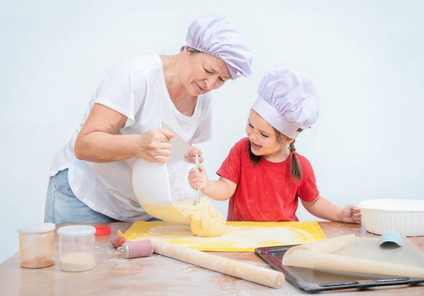 The child helps the grandmother to make bakery. Woman teaches her granddaughter to cook - Photo, Image
