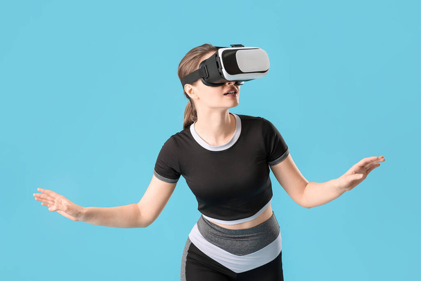 Спортивная молодая женщина в очках виртуальной реальности на цветном фоне - Фото, изображение