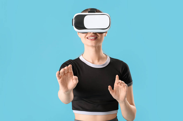 Sportliche junge Frau mit Virtual-Reality-Brille trainiert auf farbigem Hintergrund - Foto, Bild