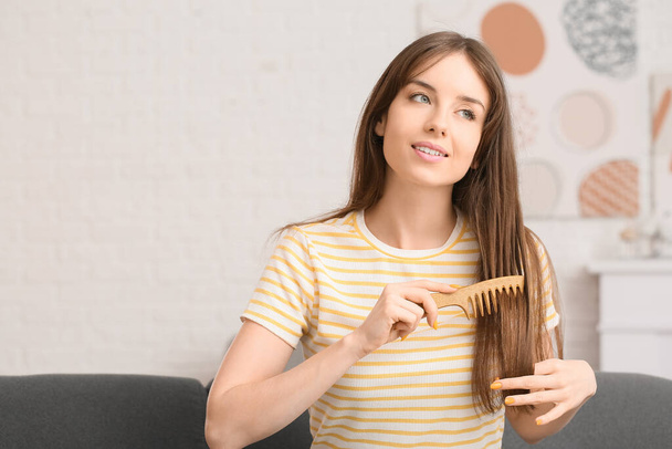 Όμορφη νεαρή γυναίκα χτενίζει τα μαλλιά στο σπίτι - Φωτογραφία, εικόνα