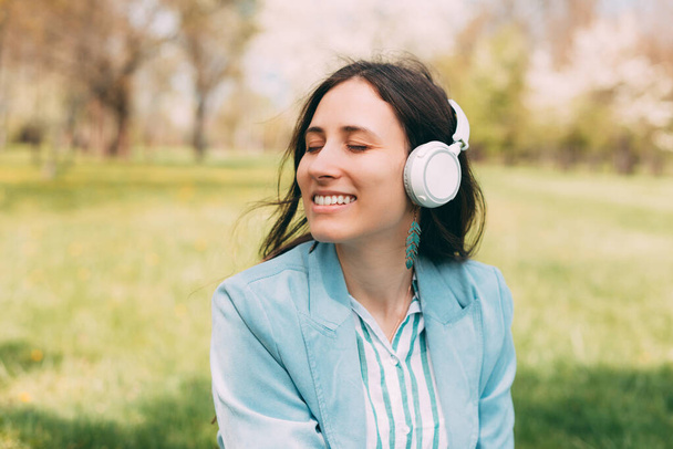 Portret van een jonge vrolijke vrouw die lacht luistert naar de muziek met haar nieuwe koptelefoon in het park . - Foto, afbeelding