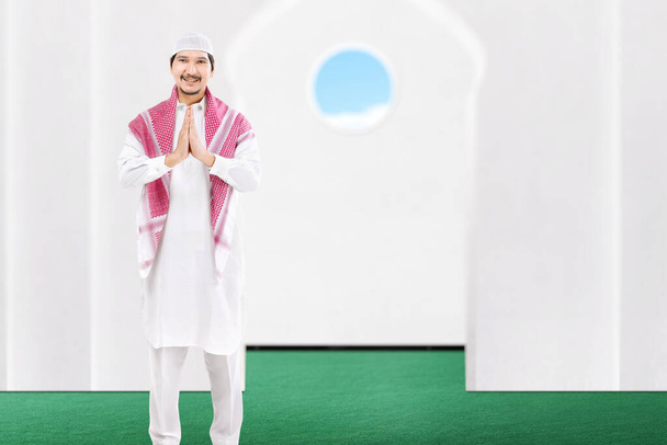 Asian Muslim man standing with greeting gesture on the mosque - Fotó, kép