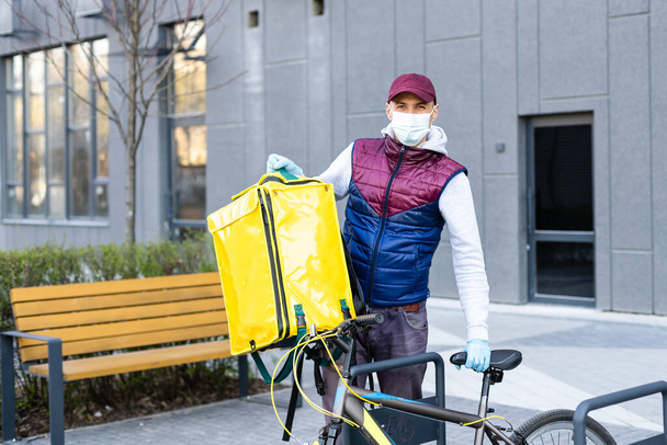 Genç kurye, şehirde bisiklet süren sarı bir termal sırt çantasıyla yiyecek getiriyor. Yemek servisi konsepti - Fotoğraf, Görsel