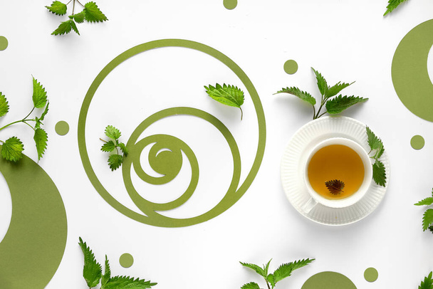 Nettle tea cup, stinging nettle herb leaves. Ornate flat lay, green paper Fibonacci sequence circles on off white background. Perfect healthy herbal tea. Alternative medicine, herbal remedy concept. - Foto, Imagen