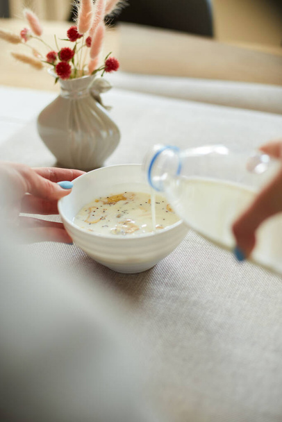 Woman Preparing Healthy Breakfast Στο σπίτι, Θηλυκό χέρι κρατώντας μπουκάλι ρίχνει γάλα σε νιφάδες δημητριακών μπολ με ξηρούς καρπούς σπόρους σταφίδες, σπίτι muesli τροφίμων βρώμης γεύμα, έννοια του τρόπου ζωής - Φωτογραφία, εικόνα