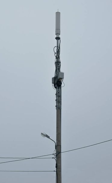 Φωτάκι δρόμου με καλώδια και κεραία ασύρματης επικοινωνίας. Ο πομπός του κινητού σήματος σε μια κολόνα. Κάθετη εικόνα. - Φωτογραφία, εικόνα