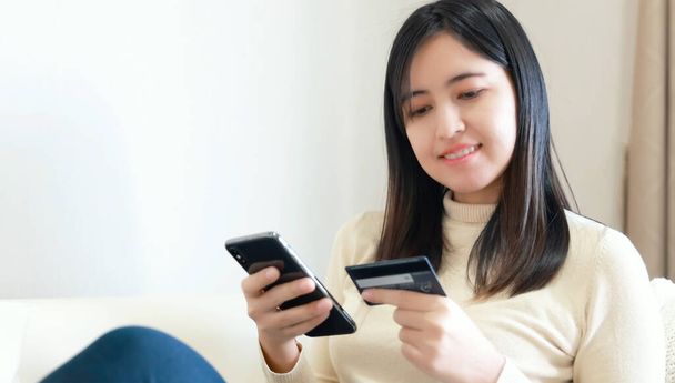 Mujer sentada en el sofá y el uso de teléfono inteligente y tarjeta de crédito para compras en línea - Foto, imagen