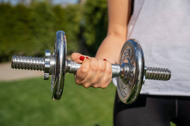 A sporty woman holding a dumbbell and working out in the park - Foto, immagini