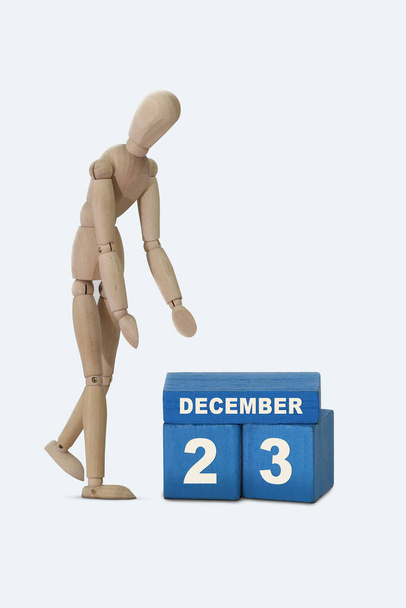 día del mes 23 Diciembre calendario Una fecha de calendario en cubos azules y un hombre de madera de pie junto a él. Fondo blanco. - Foto, Imagen