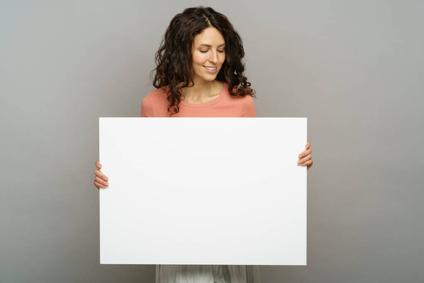 Feliz joven mujer mantenga en blanco la apariencia de pancarta para copiar el espacio con sonrisa aislada en el fondo del estudio - Foto, imagen