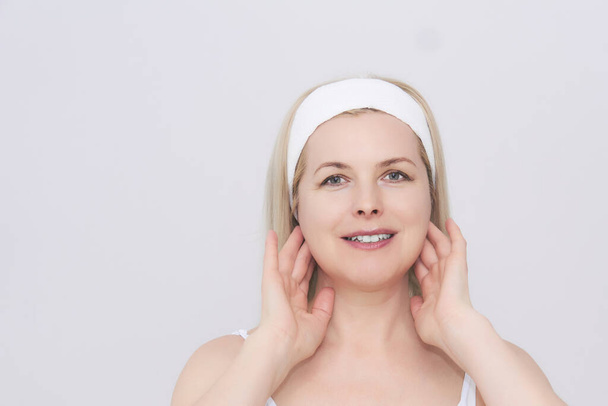 mooie vrouw van middelbare leeftijd maakt zelf-massage van het gezicht en de nek in het gebied van de lymfeklieren - Foto, afbeelding