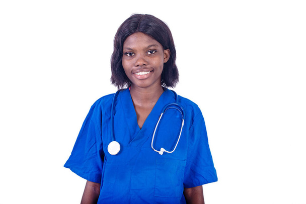 mladá sestra v uniformě stojící na bílém pozadí se stetoskopem a dívající se na fotoaparát s úsměvem - Fotografie, Obrázek
