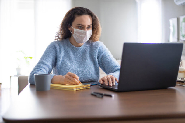 Młoda kobieta biznesu pracuje w domu w masce ochronnej po pandemi koronawirusa - Zdjęcie, obraz