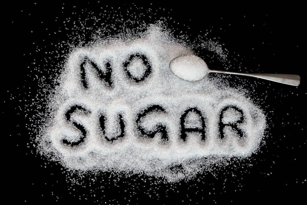 Azúcar vista superior de la imagen donde se puede leer el texto sin azúcar y la cuchara llena de azúcar sobre un fondo negro. - Foto, Imagen
