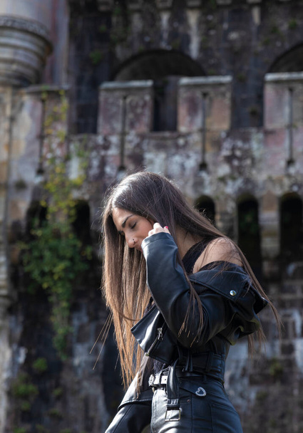 portrait of pretty young brunette woman dressed in a leather jacket in front of an old castle - Φωτογραφία, εικόνα
