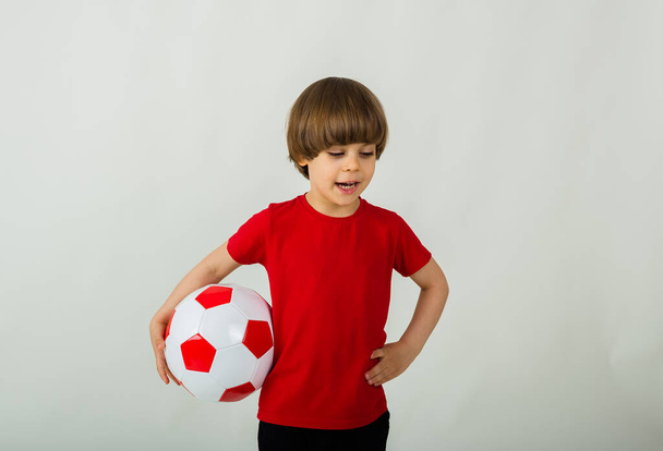 portret van een peuter jongen in een sportuniform staand met een voetbal op een witte achtergrond met ruimte voor tekst - Foto, afbeelding