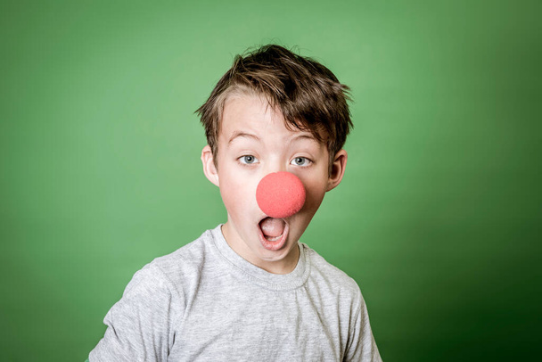 cool, cute schoolboy with green hand plaster and red clown nose is posing in front of green background - Fotografie, Obrázek