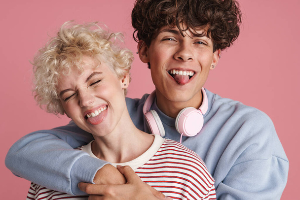 Happy young couple of teenagers standing isolated over pink background, wearing t-shirts, hugging, having fun - Φωτογραφία, εικόνα
