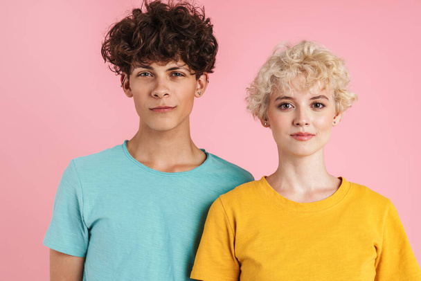 Attractive young couple of teenagers wearing t-shirts standing isolated over pink background - Zdjęcie, obraz