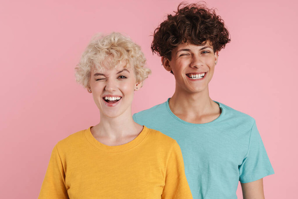 Young beautiful couple standing over isolated pink background, winking at camera - Foto, immagini